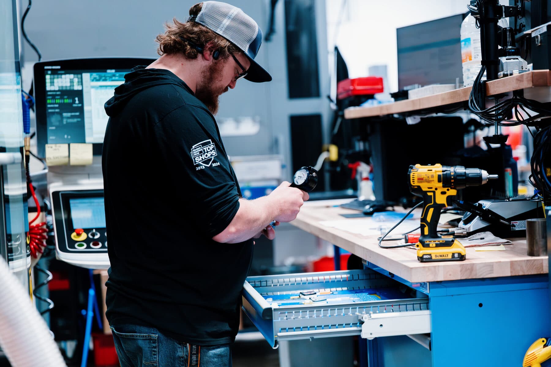 An assembly technician at a bench, hand tools and an open parts drawer beside him