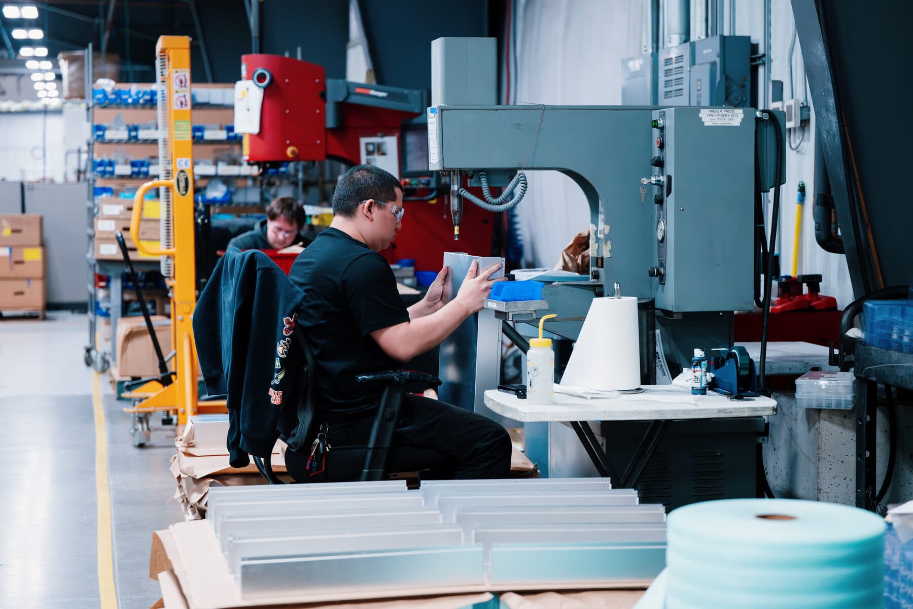 A fabricator handling a formed sheet metal part beside stacked panels