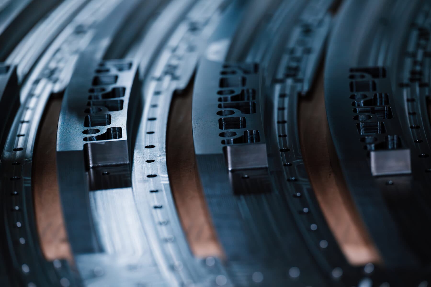 Rows of curved, slotted metal segments stacked after machining