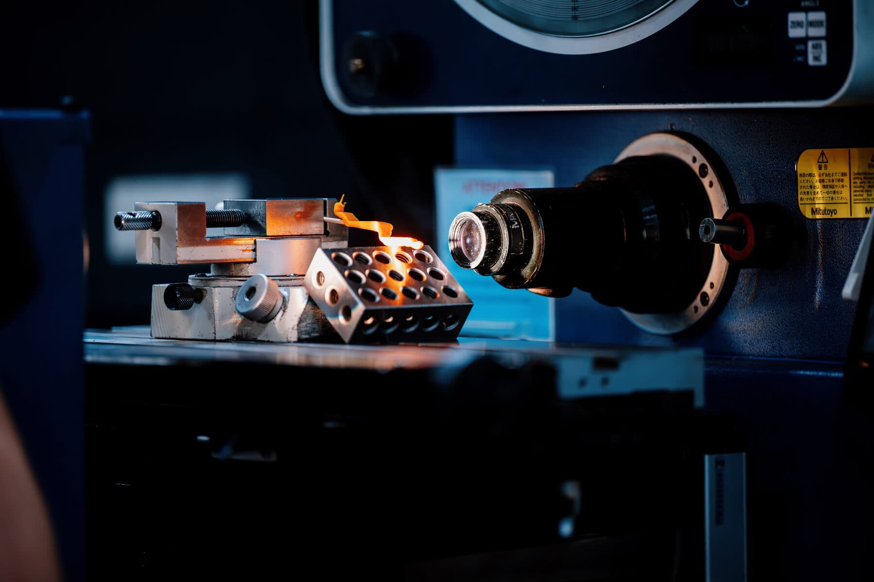 A part held in a vise in front of an optical comparator's lens